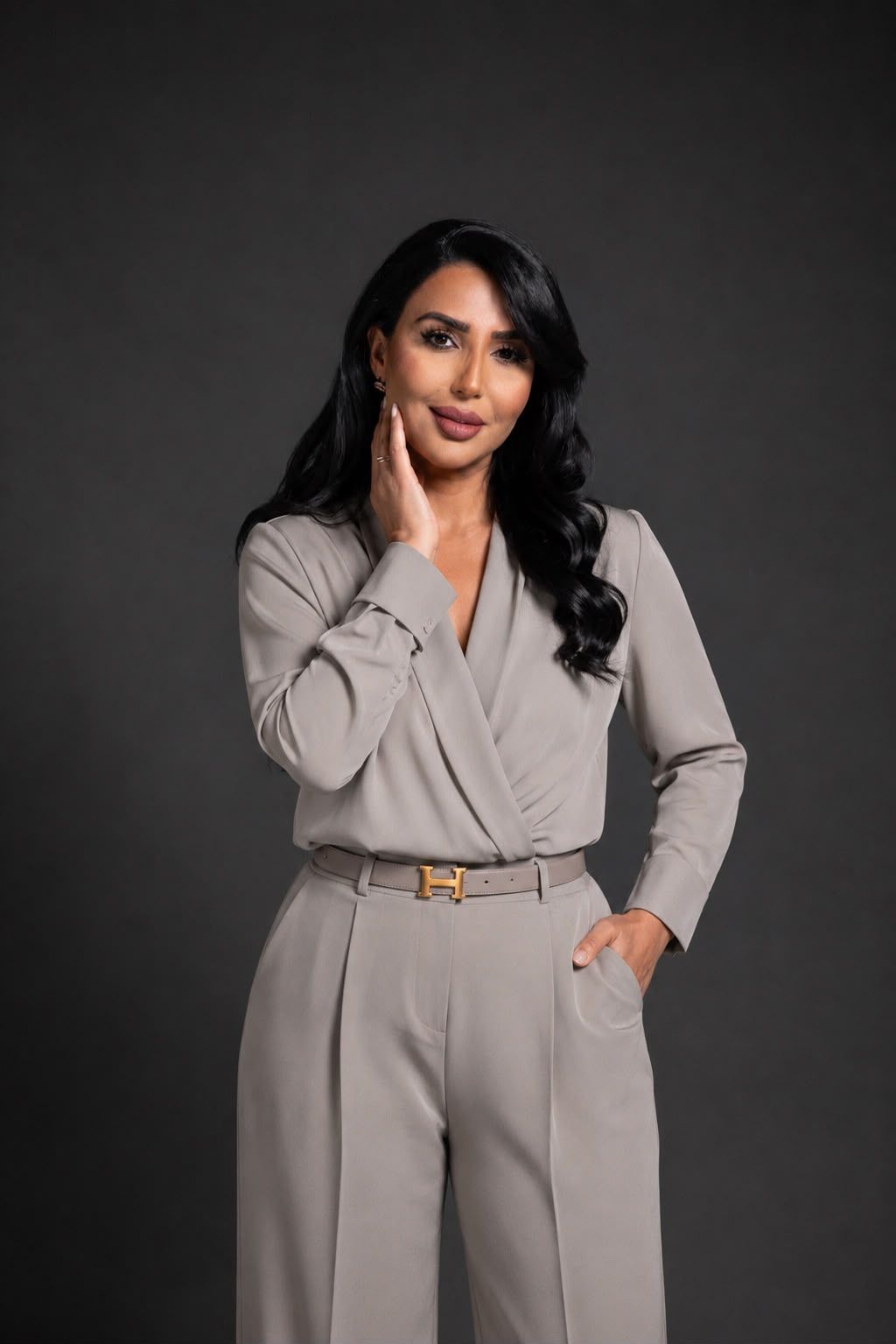 Sanaa Ouahmane in a belted stone jumpsuit against a charcoal studio wall